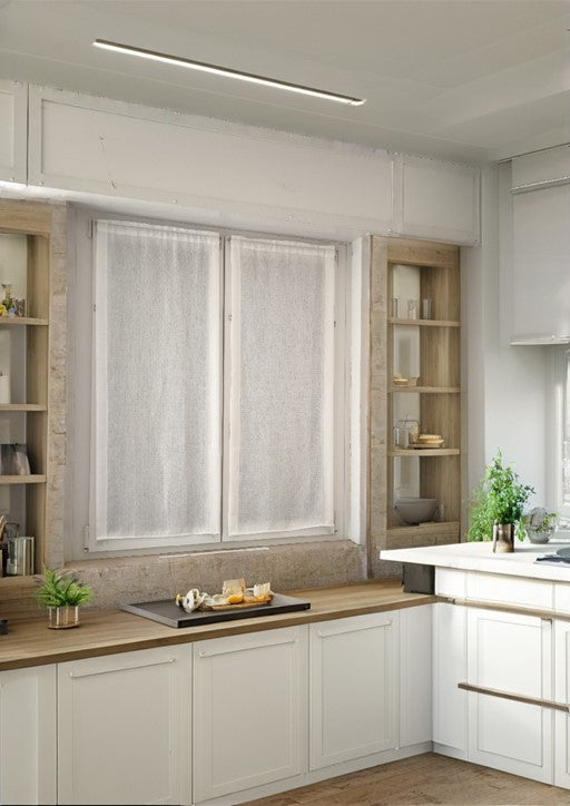 Coppia di tende bianche a vetro appese a una finestra in una cucina moderna, tessuto coprente ma luminoso.