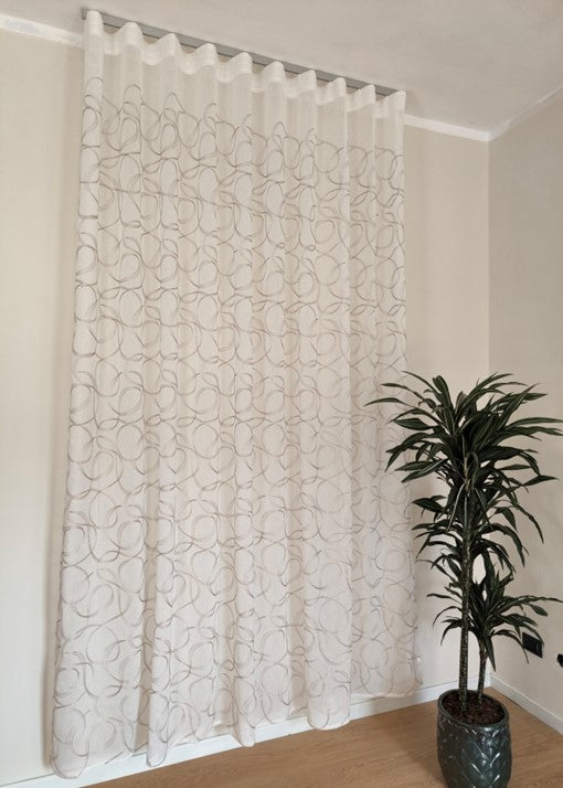 Immagine di eleganti tende a onda Wave su misura, realizzate in tessuto bianco 100% poliestere con ricamo geometrico beige, complete di un binario in alluminio satinato, ideale per un design raffinato e moderno.