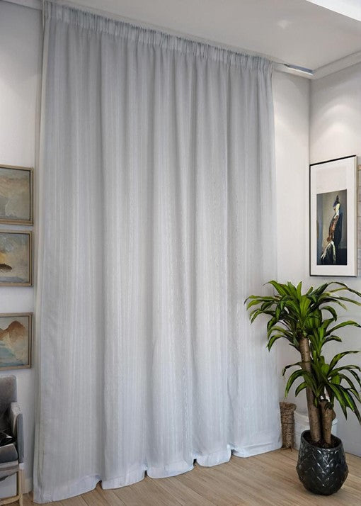 Tenda su binario montata in soggiorno moderno: una tenda grigio chiaro con fettuccia arricciata, posizionata su un binario elegante in un ambiente con mobili contemporanei.