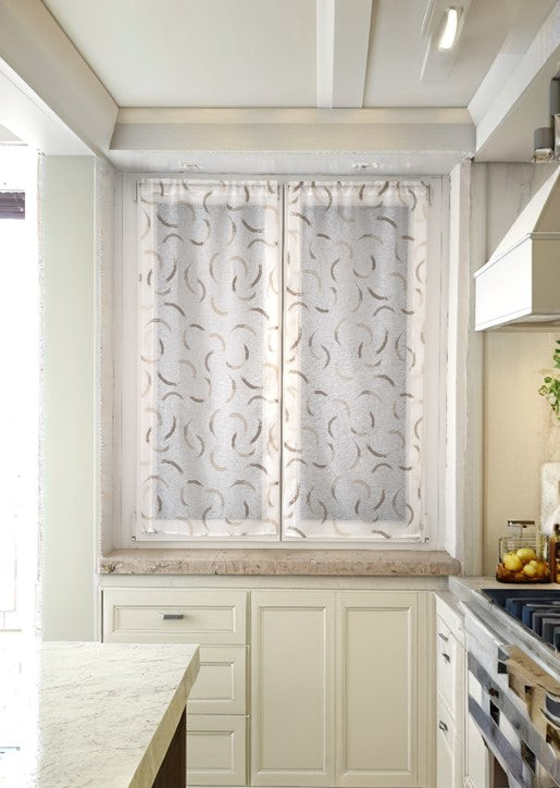 Tende a vetro beige con disegno effetto pennellate, montate su finestra in una cucina luminosa