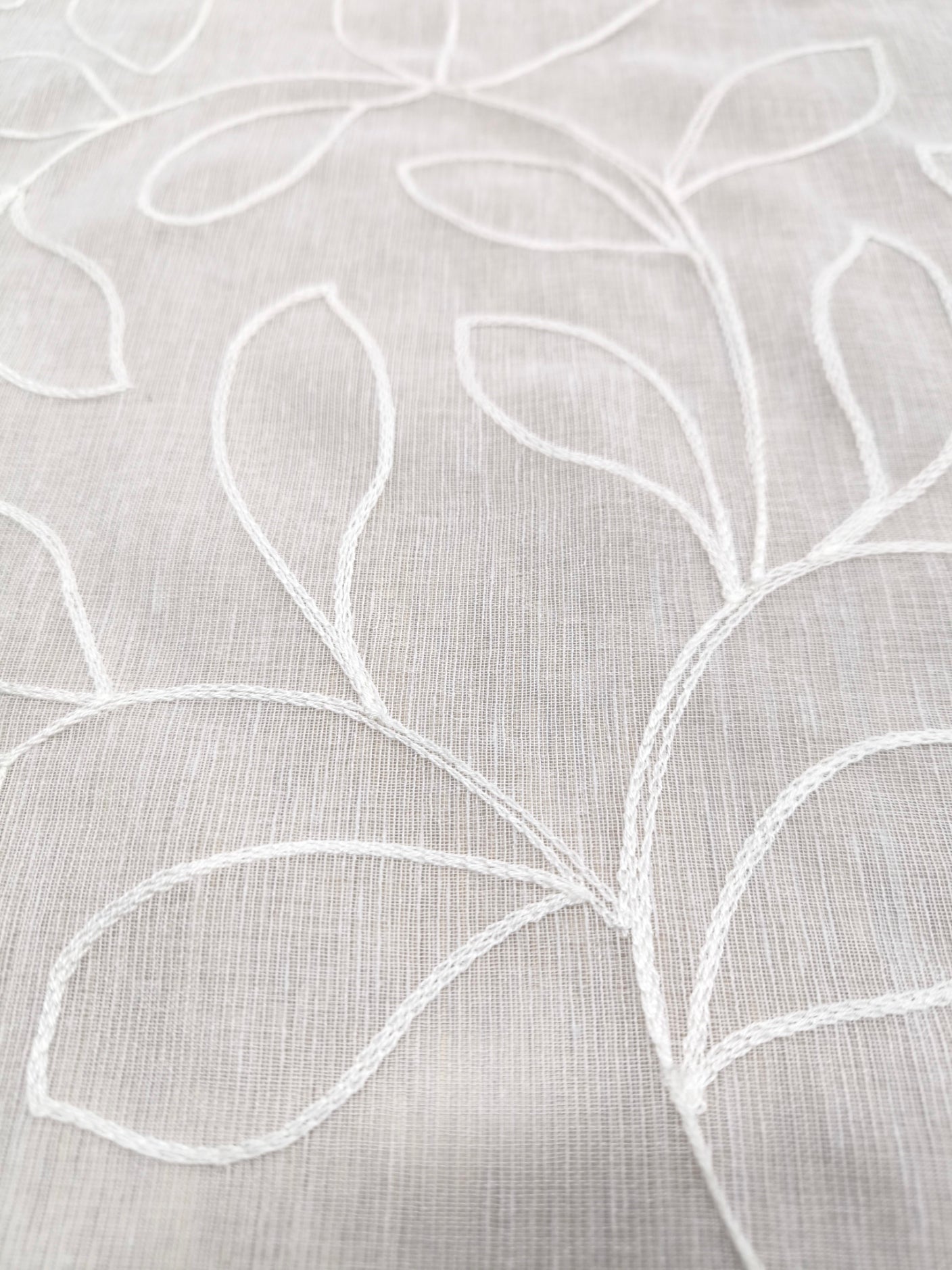 Dettaglio del ricamo a foglia su tenda bianca, evidenziando la trama e la qualità del tessuto.
